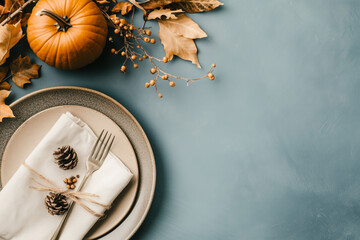 Top view of festive Thanksgiving table setting with pumpkin in plate, napkin and cutlery - autumn leaves decorated on blue background, flat lay