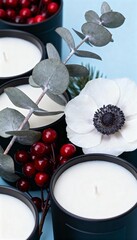 Elegant black candles with white anemone flower, eucalyptus leaves, and red berries on a light blue background