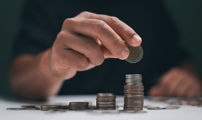 Saving money concept. Man's hand put coin on coins stack. Financial growth, investment, wealth...