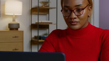 Working diligently at her laptop in a cozy home office, the woman in a red sweater is focused and engaged in her task, surrounded by a warm and orderly setting.