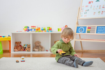 Sweet happy child boy having fun playing with cars and many colorful toys, on the floor, at home