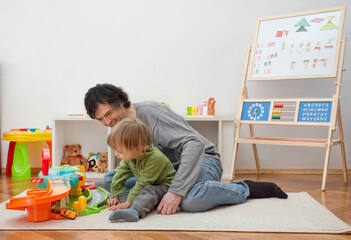 Father and sweet little child boy having fun playing with cars and colorful toys, on the floor, at home. Beautiful family moment, indoors