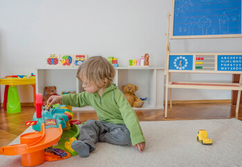Sweet happy child boy having fun playing with cars and many colorful toys, on the floor, at home