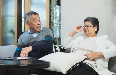 Fototapeta premium Elderly couple man and woman sit on sofa in cozy living room, use tablet together. appear be engaged in activity on tablet, possibly read browse internet plan your life, business or health insurance.