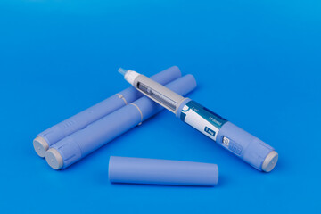 Semaglutide pens placed with pill bottles, vitamin B12 ampoules, and measuring tapes on a vibrant blue background for medical concepts.