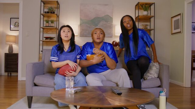 Cheering football fans in blue jerseys share intense moments of excitement and celebration while watching a thrilling game together from the comfort of their cozy living room.