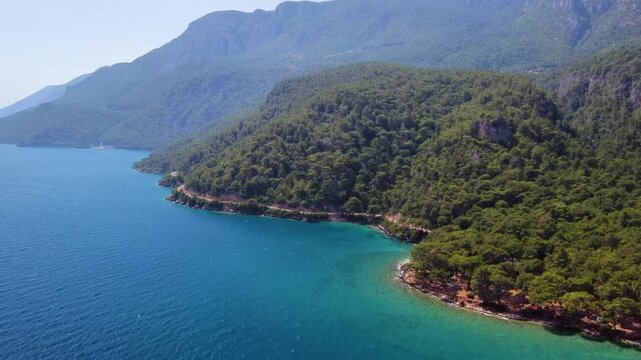 aerial footage showcasing the pristine turquoise waters and lush green hills of the Gulf of G&ouml;kova, near the charming coastal town of Akyaka in Muğla Province, Turkey. This scenic landscape highlights