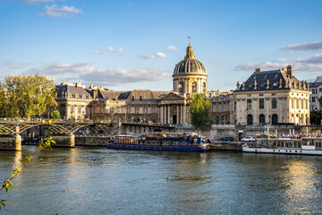 The embankment Quai de Conti with the elegant building of Institut de France facing the Seine riverbank, seen from Quai du Louvre, Paris, France.
