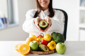 Obraz premium Nutritionist doctor holding avocado in her hands and stretching at camera, promoting healthy vegetables and fruits in nutrition, closeup