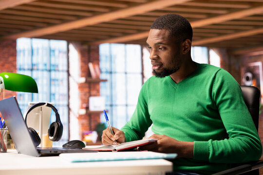 Person in home office analyzing data on notebook, writing info down on notepad, identifying trends. Freelancer using laptop compiling analytical reports, processing data, taking notes