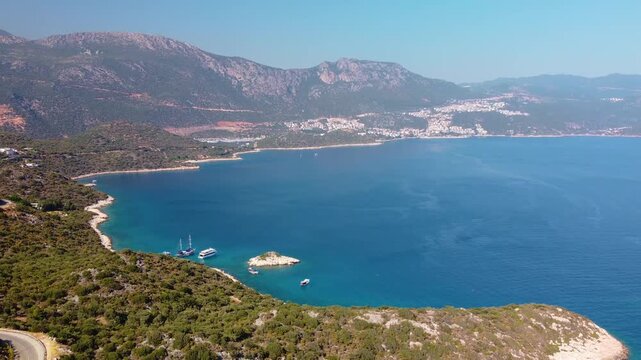aerial footage showcasing the beautiful turquoise waters and lush green coastline near Kas, a charming seaside resort town in Antalya Province, Turkey. This panoramic view captures the serene bay, dis