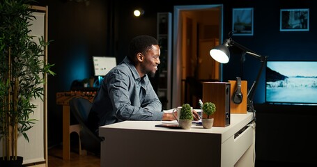 African American guy sitting at his home office and researching data, starting his day with a...