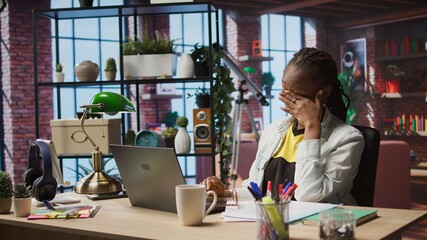 Tired teleworker yawning while typing on notebook keyboard in home office to write emails. Exhausted remote worker feeling overworked, suffering burnout while using laptop, camera A