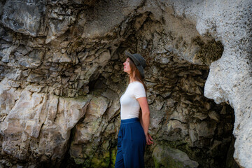 Contemplative woman in cave, looking up with a hat, wearing casual clothes