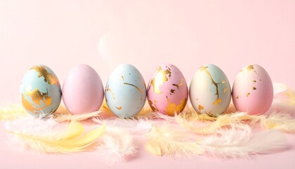 A pastel-toned arrangement of decorated Easter eggs, featuring delicate gold accents, sits amongst soft, fluffy feathers against a gentle pink backdrop.