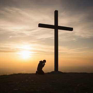 Devout person kneeling in humble prayer at the foot of a cross against a golden sunset sky