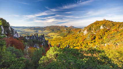 Fototapeta premium Scenic autumn landscape featuring rocky outcrops, vibrant foliage, rolling hills, and a wispy blue sky, perfect for exploration. The Sulov Rocks, national nature reserve in Slovakia, Europe.