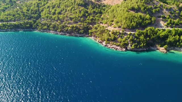 aerial footage captures the pristine beauty of the Croatian coastline, featuring a vibrant turquoise Adriatic Sea meeting lush green hills and a winding coastal road. Ideal for travel, nature, and sce