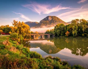 Wanddecoratie Reflectie A tranquil river scene at dawn, featuring a stone bridge arching over calm waters, reflected landscapes, and vibrant autumn foliage.  © Sarku