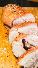 Freshly sliced roasted pork revealing juicy, tender meat inside. Half the roast remains whole with gorgeous golden crackling, while beautiful succulent slices lay beside it on a wooden board.