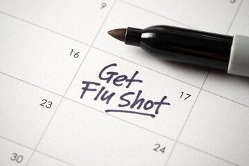 A close-up of a calendar with a handwritten note saying Get Flu Shot, serving as a reminder for an important health appointment. A symbol of influenza prevention and personal healthcare planning