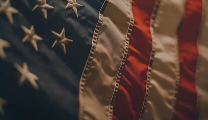 Close-up of the American flag, highlighting its intricate design and vibrant colors. The focus is on one corner with a blurred background that suggests an open space for text or imagery.