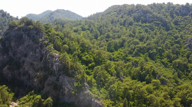 aerial drone footage captures the natural beauty of the forested mountains surrounding Turunc, a picturesque coastal town in Turkey. This serene landscape features dense green trees, rugged terrain, a