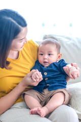 Asian woman with her son holding him by her hand. Happy asian baby boy was holding by his mother. Asian family with little boy at home enjoy tender carefree family moment, motherhood