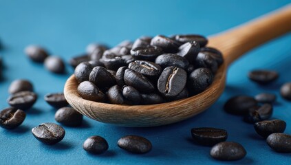 Close-up of roasted coffee beans in a wooden spoon and scattered, against a blue backdrop