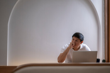 Asian freelancer thinking and working on laptop at home