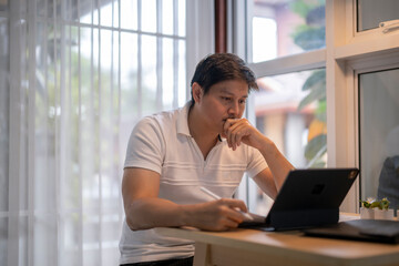 Focused asian freelancer working from home using tablet and pen