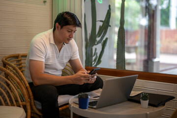 Asian freelancer using smartphone and laptop in cafe