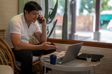 Asian freelancer talking on phone and working on laptop in cafe