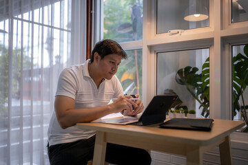 Asian freelancer working from home using tablet and drinking coffee
