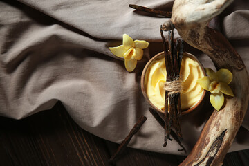 Composition with bowl of tasty pudding, vanilla sticks, tree branch and fabric on dark wooden table