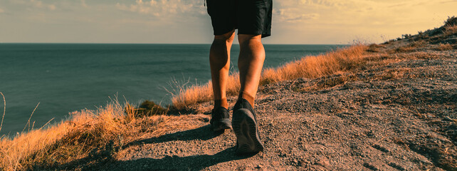 A man takes a brisk walk outdoors on a trail located on an elevated area overlooking the sea or ocean. A close-up view from behind.