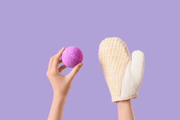 Female hands with bath bomb and massage glove on lilac background, closeup