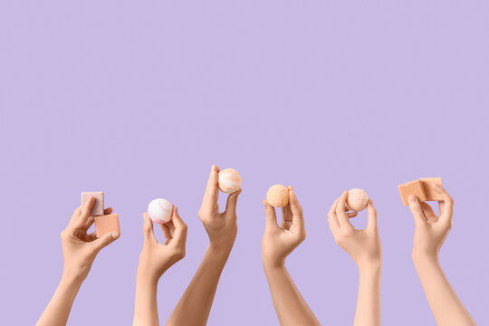 Female hands with different bath bombs and soap bars on lilac background