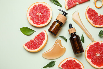 Composition with bottles of cosmetic products, facial massage tools and slices of grapefruit on green background, closeup