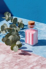 Small glass jar with pink and white striped sand, beside eucalyptus leaves on a two-toned surface