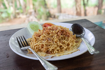 Delicious plate of fried noodles with fresh garnish. Quick meal, fried noodles with cucumber and tomato. Savory instant noodles with crispy onions on top. Flavor-packed fried noodles