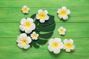 Obraz premium Beautiful plumeria flowers and decorative monstera leaf on green wooden background