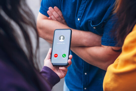 Close-up of a smartphone with an incoming call screen, held during a group interaction. Concept modern communication, social connection, and digital lifestyle with people engaged in conversation.