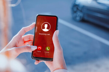 Woman hand with painted nails is seen using a smartphone to either Accept or Decline an incoming call on an urban street on a parking.