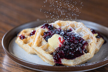 Golden waffles topped with fresh huckleberries, berry jam, and a pat of butter while powdered sugar...