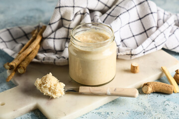 Marble tray, napkin, glass jar and spoon with horseradish sauce on blue grunge background, closeup