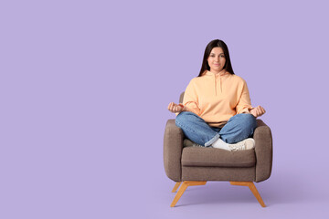 Young woman meditating in armchair on lilac background. Zen concept