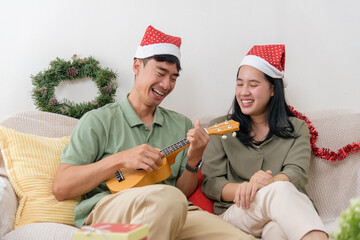 Christmas holiday brings happy couple love, enjoying festive winter celebration at home, man plays ukulele, woman listens, cheerful christmas decorations adorn cozy living room