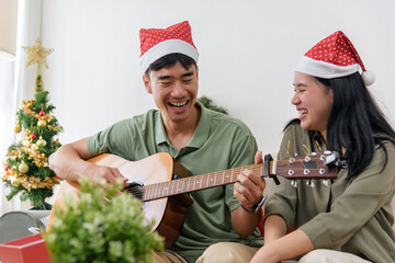 Christmas couple shares love, happy holiday winter moment with music as man plays guitar for woman wearing santa hats, enjoying cheerful festive christmas celebration at cozy home