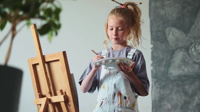 Young painter developing her imagination while painting with focus. Art as learning method for kids at home. Promotes positive childhood and creative thinking in modern setting